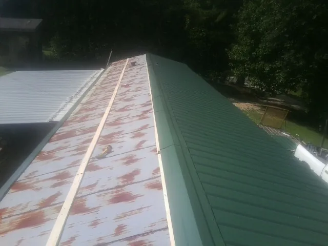 Old rusted panels beside newly installed green metal roofing — Wind Damage Roof Repair by Roofing Brothers in Blountstown