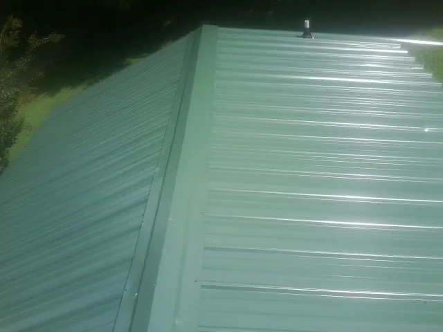 New green metal panels meeting at the ridge of a roof — Flat Roof Repair work by our crew in Blountstown