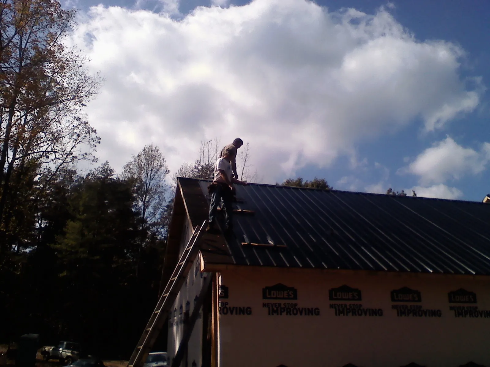 Roofer fastening dark metal panels high against a cloudy sky, from a Roof Inspection job in Blountstown